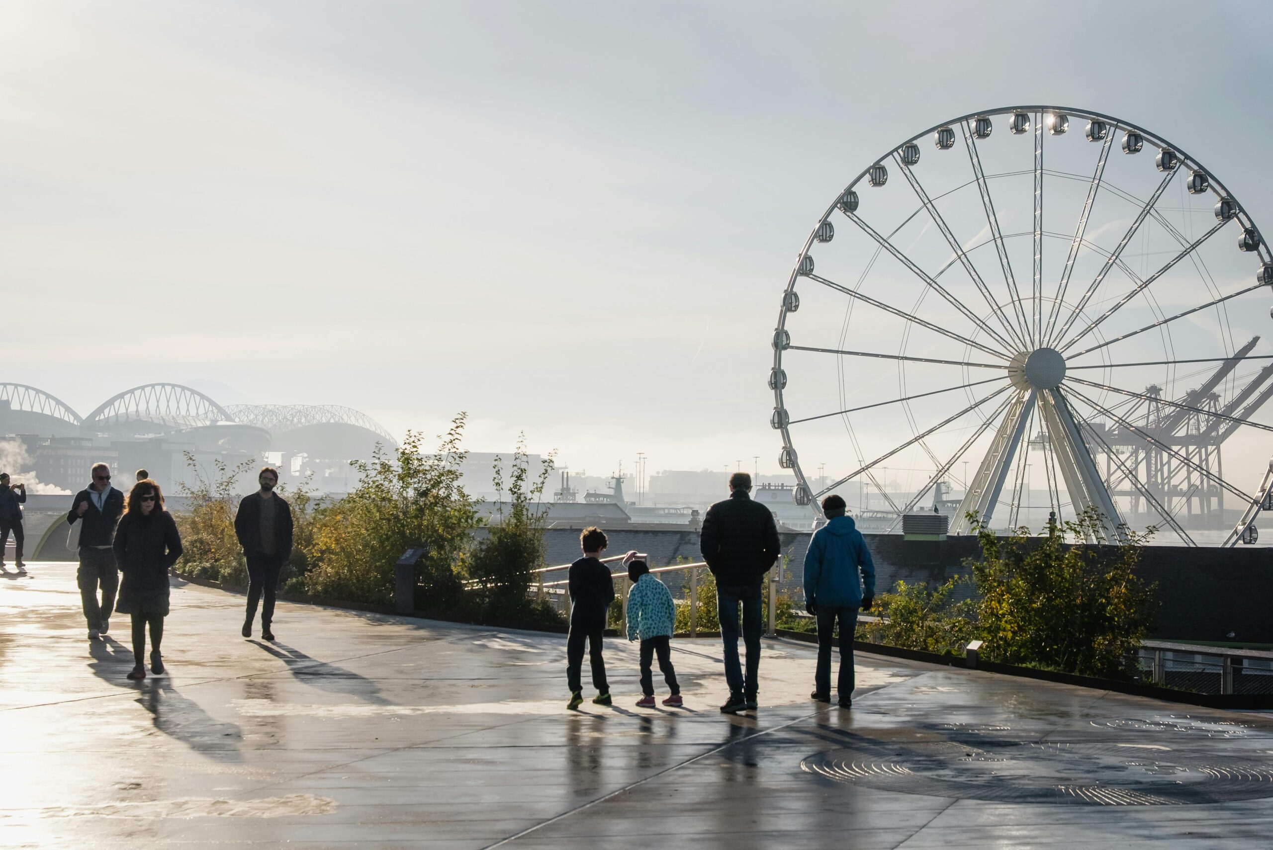 Eine Gruppe von Menschen spaziert in der Abendd&Atilde;&curren;mmerung am Wasser entlang, im Hintergrund ist das Seattle Great Wheel zu sehen.