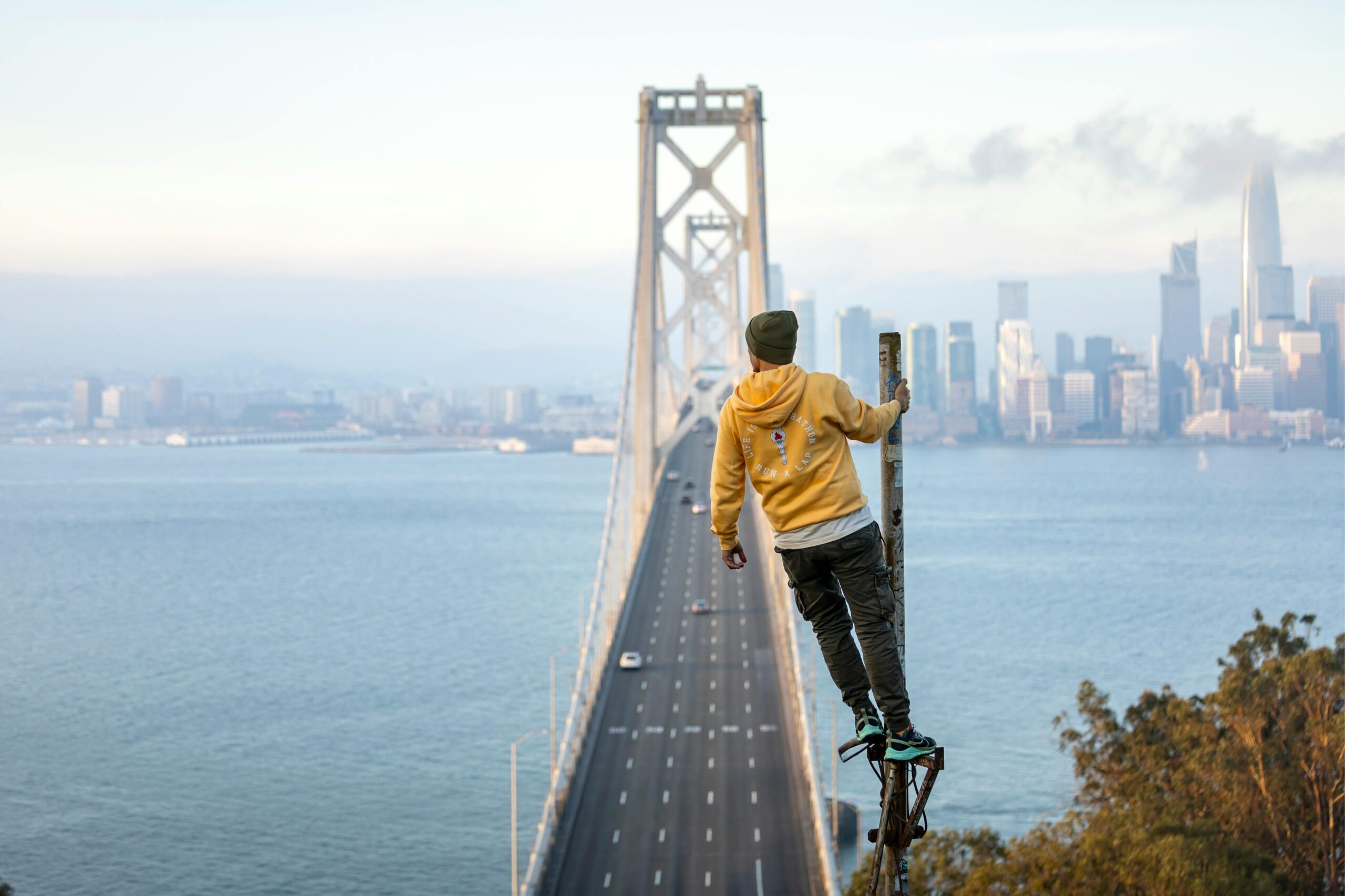 Eine Person steht auf einem Pfahl und hat einen atemberaubenden Blick auf die San Francisco Bay Bridge und die Skyline der Stadt.